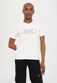 White cotton T-shirt featuring a silver rhinestone logo in the center and short sleeves. The fit is relaxed, with a round neckline.