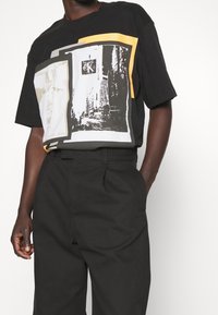 Svart t-shirt med abstrakta grafiska mönster i beige, grått och gult. Korta ärmar, avslappnad passform och rundad hals.