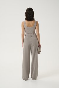 Débardeur avec des détails d'épaules cloutés en gris clair, assorti à un pantalon large de la même teinte, tenant un petit sac texturé.