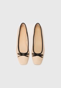 Beige ballet flats with a square toe, black trim around the opening, and black bows on the front. Smooth texture, simple design.