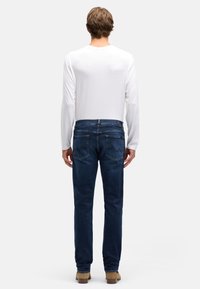 Ciemnoniebieskie dżinsy z denimu o wąskim kroju i lekkim rozciągnięciu, z tylnymi kieszeniami ozdobionymi subtelnym szwem, noszone z białą koszulą z długim rękawem.