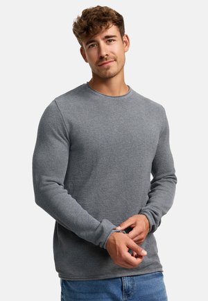 Camisa gris de manga larga con un patrón de tejido texturizado, escote redondo y puños ajustados, combinada con jeans azules.