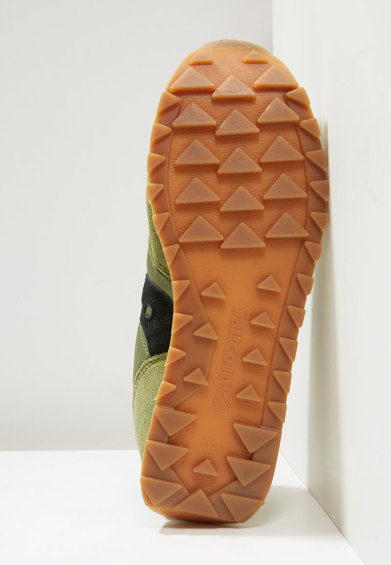 Groene suede hardloopschoen zool met een oranje rubberen basis, voorzien van triangulaire loopvlakken voor grip en een zwart accentband.