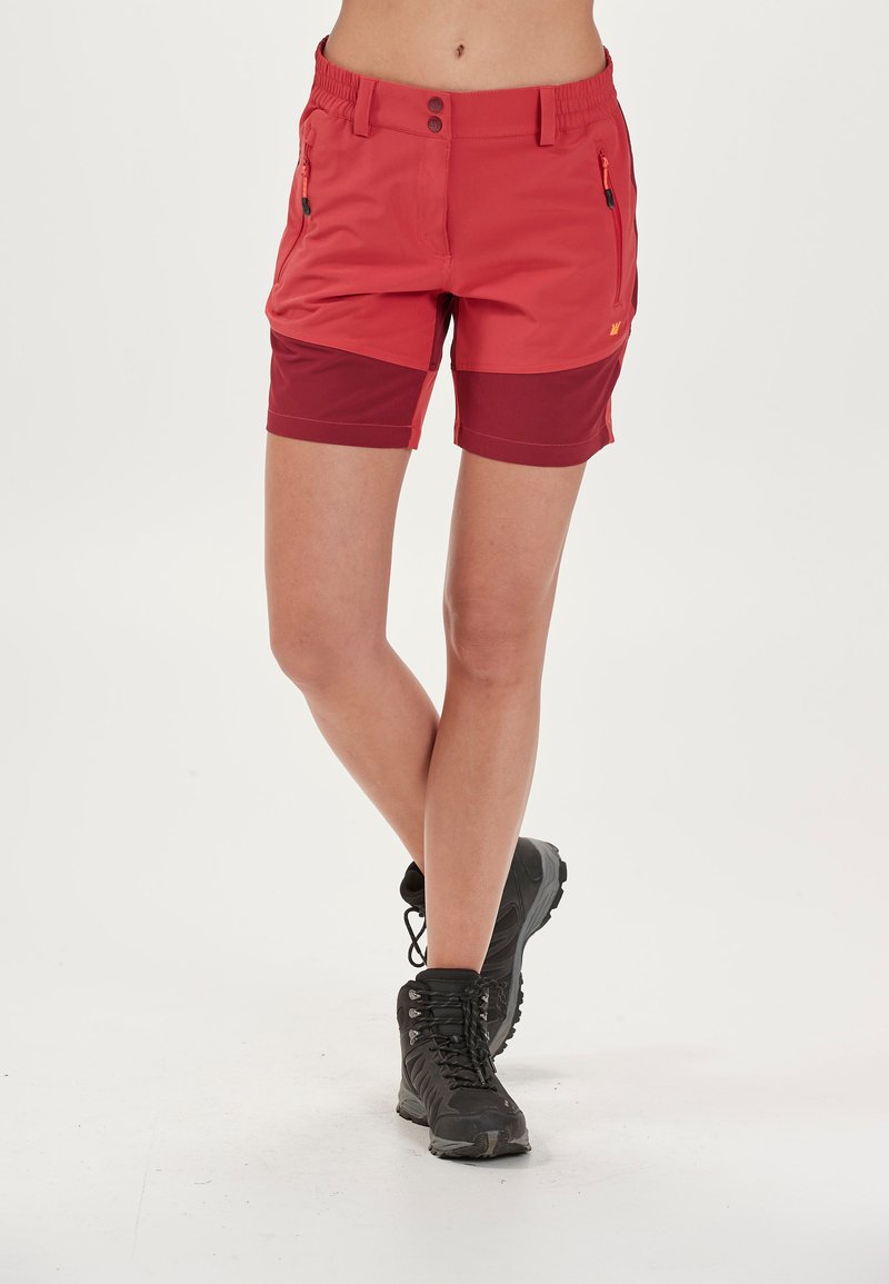 Röda vandringsshorts med en mörkare röd panel, elastisk midja, knäppning och dragkedjefickor; bärs med svarta vandringskängor.