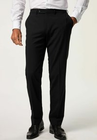 Pantaloni neri con una texture liscia, taglio slim e pieghe frontali. Caratterizzati da una chiusura con bottone e tasche, abbinati a scarpe nere lucide.