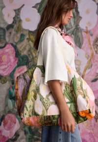 Stor skuldertaske med blomsterprint i pink, grøn og orange. Fremstillet af stof med håndtag i naturlig tone. Har et rummeligt, slasket design.