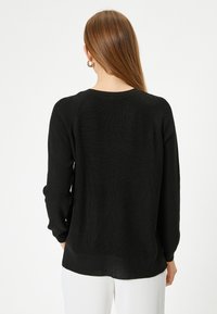 Maglione nero lavorato a maglia con vestibilità comoda, maniche raglan e texture a costine. Presenta un colletto a girocollo e un orlo posteriore leggermente più lungo.