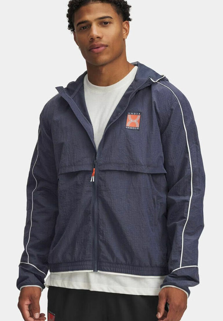 Veste légère à capuche marine avec une fermeture éclair à l'avant, des rayures blanches et un patch logo orange. Tissu texturé et coupe décontractée.