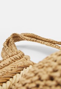 Geflochtene Strohtasche mit langen Griffen. Natürliche Tan-Farbe. Strukturierte Oberfläche mit sichtbaren Webmustern. Verstellbare Riemenlänge.