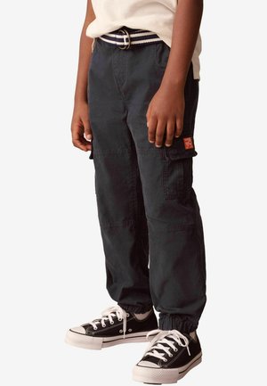 Pantalones cargo negros con un ajuste relajado, que cuentan con bolsillos laterales y puños elásticos, combinados con zapatillas negras y un cinturón a rayas.