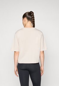 Beige crop top met korte mouwen en een ronde halslijn, gemaakt van zachte stof, gecombineerd met zwarte broek. Geen zichtbare patronen of accenten.