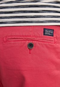 Rode katoenen broek met een achterzak met een zwarte knop en een label met de tekst "Petrol Ind." Gestreepte stof steekt bovenuit.