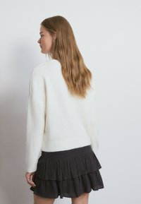 Suéter blanco de corte relajado, con mangas raglán y dobladillo acanalado, combinado con una falda negra de volantes en capas. Textura suave, diseño minimalista.