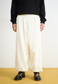 White wide-leg pants made from soft fabric, featuring an elastic waistband and paired with black chunky-soled boots with a patterned accent.