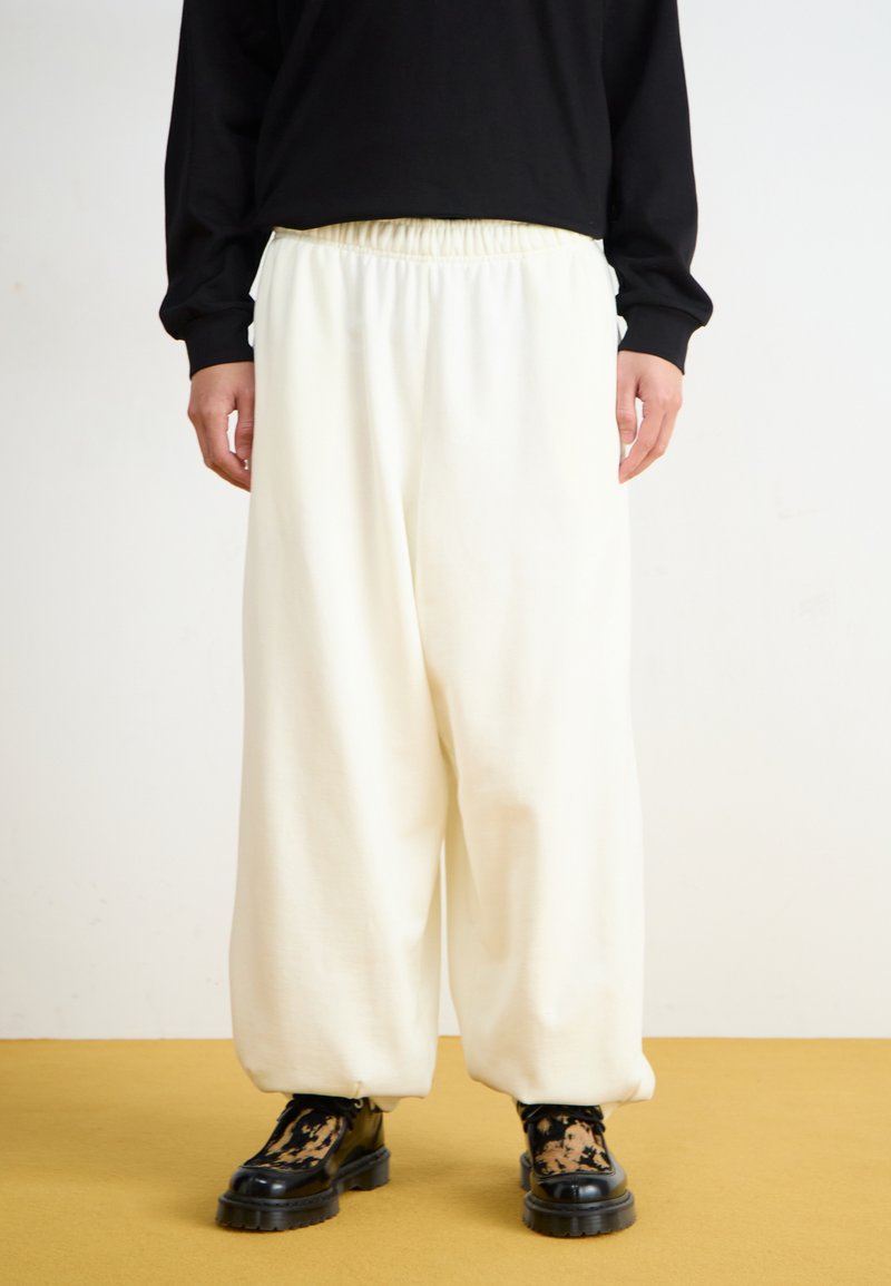 White wide-leg pants made from soft fabric, featuring an elastic waistband and paired with black chunky-soled boots with a patterned accent.