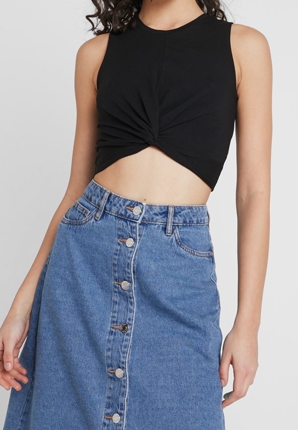Haut court noir sans manches avec un détail torsadé à l'avant, associé à une jupe en jean bleu mi-longue avec une patte de boutonnage à l'avant et des poches.