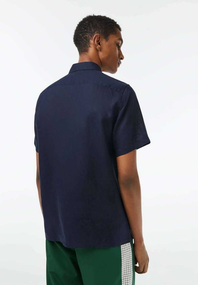 Camisa de manga corta en color navy, hecha de una tela suave, con un cuello clásico y un corte recto, vista desde la parte de atrás.