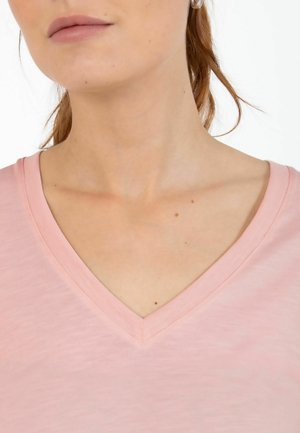 Hellrosa V-Ausschnitt-T-Shirt, weicher Stoff, gerippter Halsausschnitt, sichtbare Hautstruktur mit leichten Sommersprossen und unauffälligem Hintergrund.