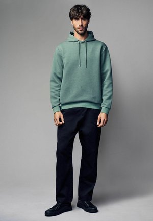 Felpa con cappuccio in tessuto verde chiaro testurizzato, abbinata a pantaloni neri e sneakers nere. Taglio dritto, cordoncino al cappuccio.