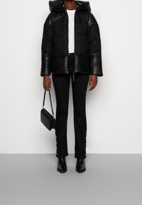 Černá prošívaná bunda s lesklým koženým povrchem a kapucí, s prošívaným designem. Kombinována s černými kalhotami a šněrovacími botami na podpatku.