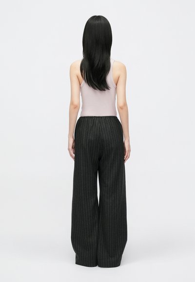 Zwarte pinstripe wijde broek met een gestructureerde afwerking. Gecombineerd met een lichtpaars mouwloos topje, weergegeven van de achterkant.