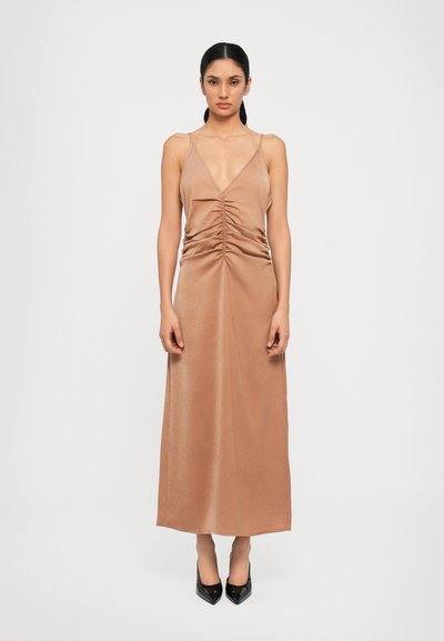 Long, sleeveless dress in a soft, light brown fabric with a deep V neckline and gathered detail at the waist. Smooth texture and floor-length.