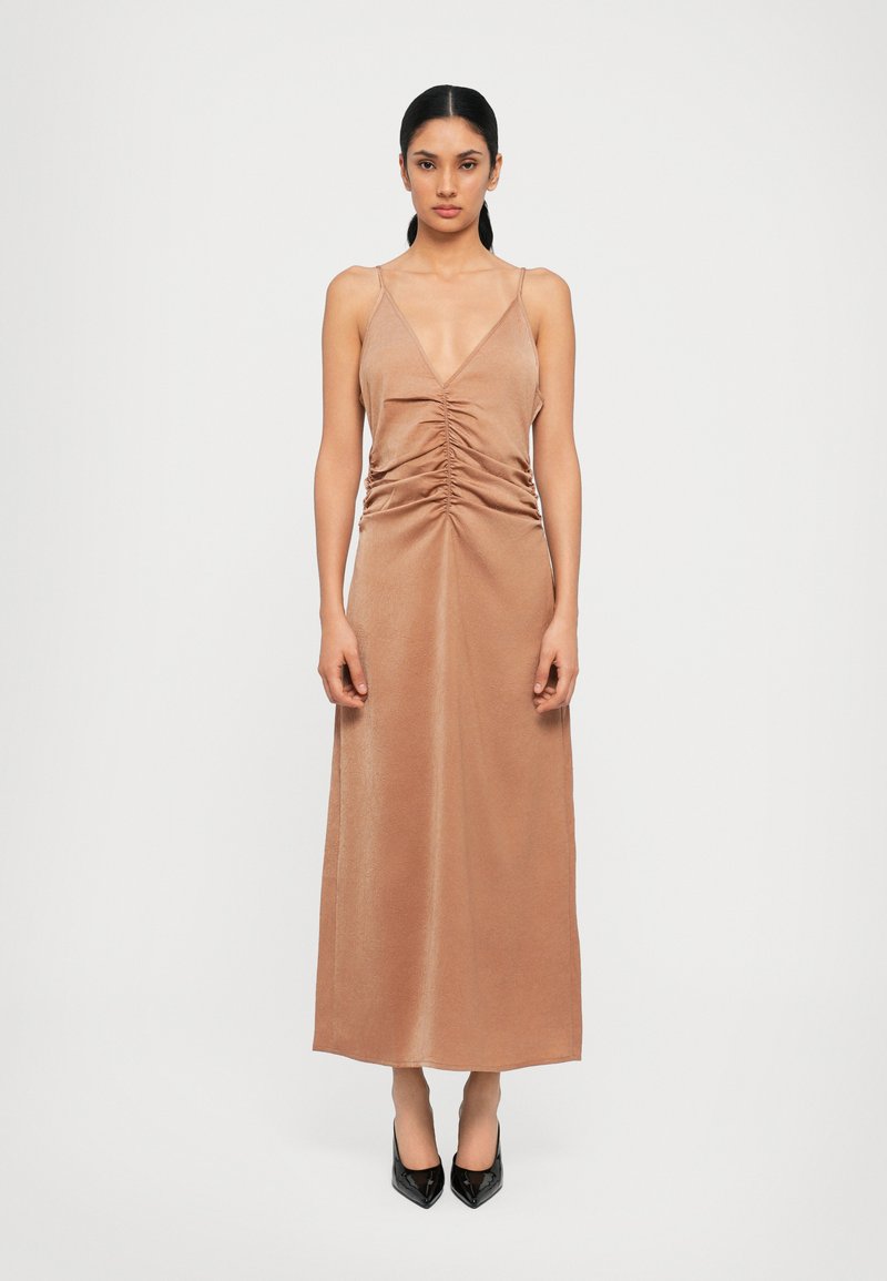 Long, sleeveless dress in a soft, light brown fabric with a deep V neckline and gathered detail at the waist. Smooth texture and floor-length.