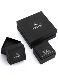 Svarta papperslådor i olika storlekar med en matt yta, som visar "Kuzzoi"-logotypen på en etikett och produktionsdetaljer på den minsta lådan.