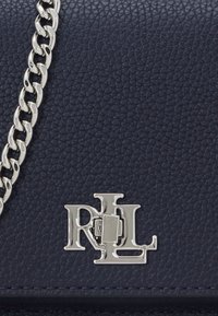 Bolso cruzado de cuero azul marino con un acabado texturizado, que presenta una cadena plateada y un prominente cierre de logotipo plateado.