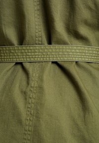 Olive green fabric with a smooth texture, featuring a stitched belt and gathered detail. The design includes clean lines and subtle sheen.
