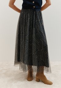 Jupe maxi en motifs géométriques bleu marine et crème, fabriquée en tissu léger et transparent, dotée d'une taille à cordon de serrage et associée à des bottes à talons marron.