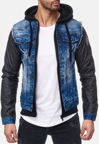 Veste en denim et simili cuir avec une palette de couleurs bleu et noir, dotée d'une capuche, de poches poitrine boutonnées et de détails usés sur les épaules.