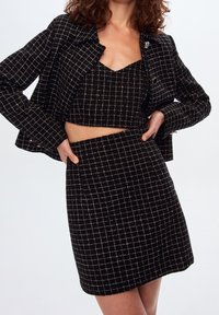 Zwart geruit co-ord set bestaande uit een cropped jasje, mouwloze top en rok met een rasterpatroon, gestructureerde stof en zilveren accenten.