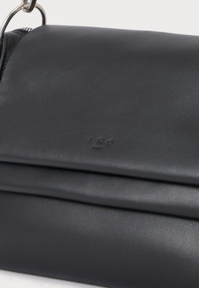 Sac à main en cuir noir avec fermeture à rabat et marquage embossé subtil, avec un détail d'anneau métallique sur la bandoulière.