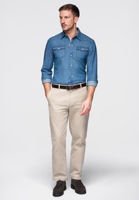 Chemise en jean à manches longues, deux poches poitrine et col boutonné ; associée à un pantalon chino beige et des chaussures foncées. Design simple et décontracté.