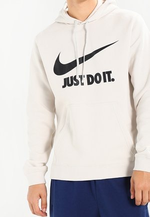 Lichtbeige hoodie met een zwart Nike swoosh logo en de tekst "JUST DO IT." Gemaakt van zachte stof, met een kangoeroezak en een capuchon met trekkoord.