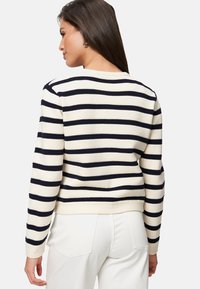 Pull rayé avec des bandes crème et bleu marine, texture côtelée, manches longues et col rond, associé à un pantalon blanc.