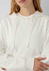 Biała bluza z kapturem ze sznurkiem, z nadrukowanymi sznurkami. Miękka, fakturowana tkanina o luźnym kroju i długich rękawach.