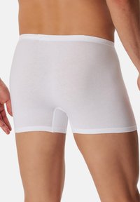 Boxer-briefs blancs en coton avec un design ajusté, présentant une texture douce, une taille élastique et une longueur de jambe courte.