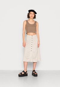 Top cropped castanho, saia A-line bege com botões frontais e sandálias plataforma pretas grossas. Boina preta como acessório.