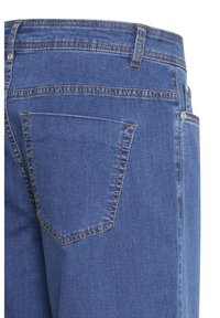 Vedere din spate a blugilor din denim albastru, cu buzunar cusut, bucle pentru curea și detalii cu nituri pe buzunarul lateral.