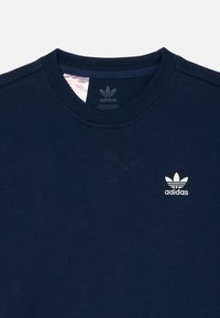 Tumszils kokvilnas maisījuma džemperis ar apaļu kaklu, ribotu aproču un apakšmala, kā arī baltu izšūtu Adidas logotipu uz krūtīm.