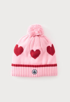 Bonnet en tricot rose avec trois cœurs rouges, un pompon sur le dessus et un petit logo rond sur le bord côtelé.