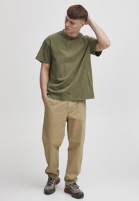 Oliven grønn oversized bomull T-skjorte, beige avslappet bukser, og grå tursko med sorte detaljer. Enkle teksturer og minimalistisk design.