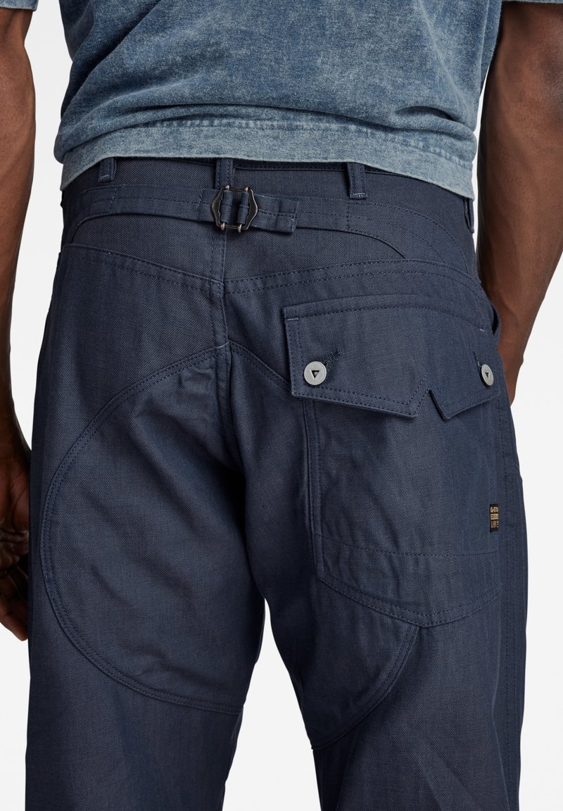 Marineblauwe broek met een ontspannen pasvorm, voorzien van meerdere zakken, versterkte stiksels en een textuurfinish. Verstelbare taille.