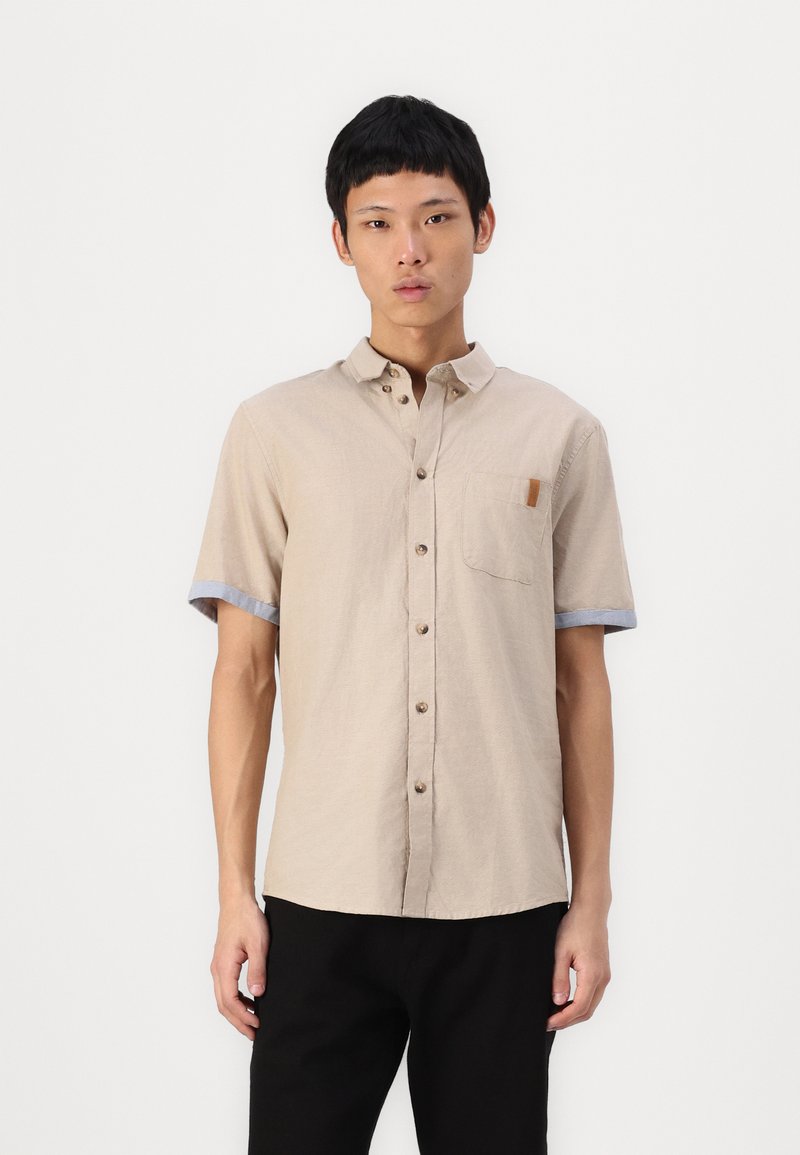 Camisa beige de manga corta con botones en el frente, bolsillo en el pecho y acentos azul en los puños. Fabricada con una tela texturizada y un ajuste relajado.