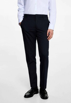 Marineblauwe broek van soepel materiaal met een op maat gemaakte pasvorm, met zijzakken en een nette plooi aan de voorkant. Zwarte formele schoenen complementeren de look.