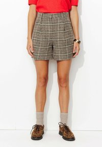Shorts à carreaux marron avec une taille haute, présentant une coupe structurée. Associés à des chaussures à imprimé animal et des chaussettes grises arrivant aux genoux.