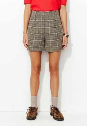 Shorts à carreaux marron avec une taille haute, présentant une coupe structurée. Associés à des chaussures à imprimé animal et des chaussettes grises arrivant aux genoux.