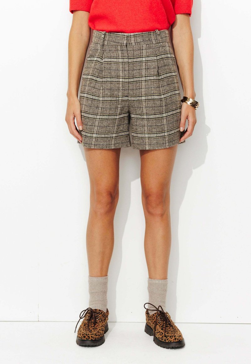 Shorts à carreaux marron avec une taille haute, présentant une coupe structurée. Associés à des chaussures à imprimé animal et des chaussettes grises arrivant aux genoux.